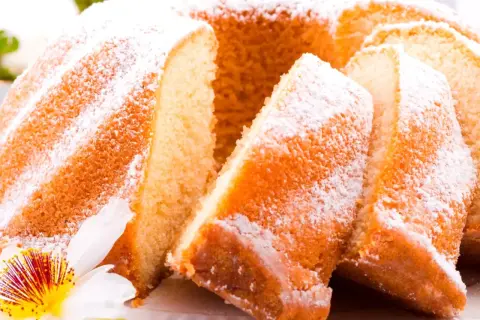 Puszysta babka wielkanocna, oprószona cukrem pudrem, z kawałkami ciasta i kwiatową dekoracją.