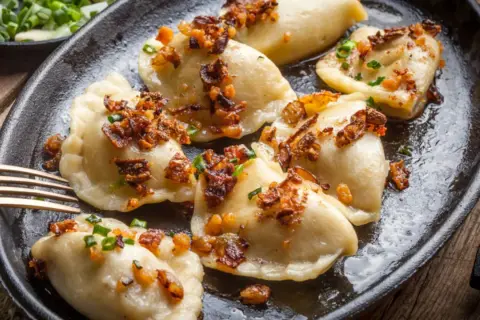 Pyszne pierogi z mięsem mielonym, okraszone skwarkami i szczypiorkiem, podane na żeliwnej patelni.