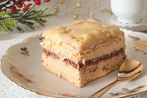 Pyszne ciasto z budyniem, przełożone kremem i polane lukrem. Idealne na święta, z gałązką choinki w tle.