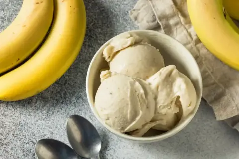 Pyszne lody bananowe w miseczce, obok świeże banany i łyżeczki. Idealne na upalny dzień.