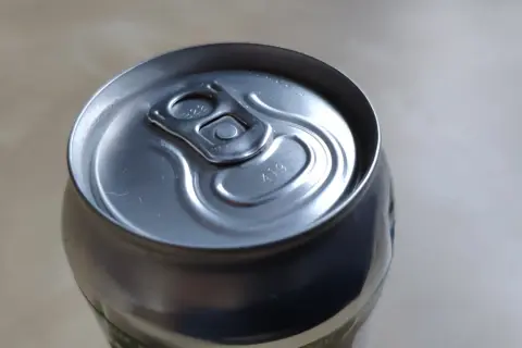 Metalowa puszka piwa z widocznymi kropkami na wieczku, które mogą oznaczać datę produkcji lub numer partii.