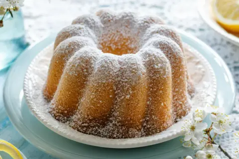 Puszysta babka cytrynowa oprószona cukrem pudrem, ozdobiona gałązką kwitnącej wiśni. Idealna na wiosenne popołudnie.