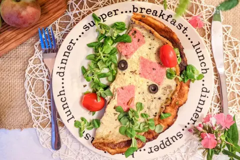 Pyszne, sycące śniadanie do pracy: omlet z szynką, pomidorkami i oliwkami, udekorowany świeżą sałatką.