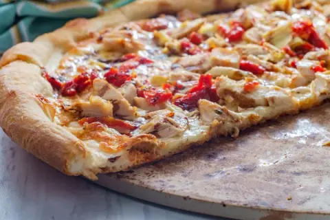 Pyszna pizza włoska z kurczakiem i suszonymi pomidorami, z chrupiącym brzegiem, na kamieniu do pieczenia.