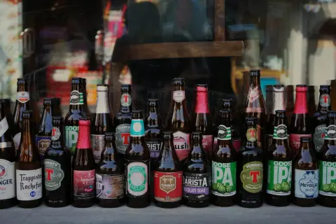 Rząd butelek po piwie, w tym Goose Island, Chimay i Lindemans. Możliwy zwrot butelek po piwie bez paragonu.