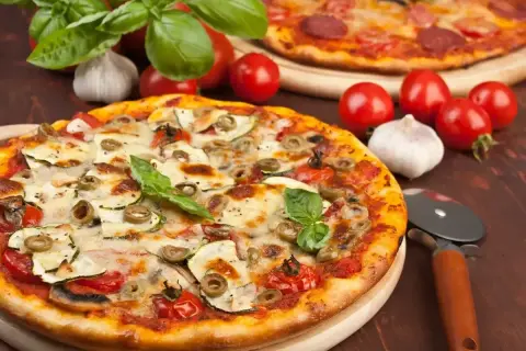Pyszna pizza z cukinią, oliwkami i pomidorkami, obok surowe pieczarki na pizze, czosnek i bazylia.