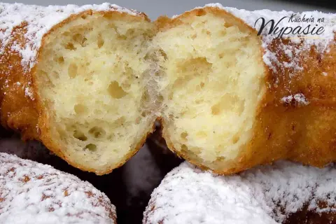 Puszyste oponki serowe, przekrojone na pół, obficie posypane cukrem pudrem. Widać ich delikatne, pęcherzykowate wnętrze.