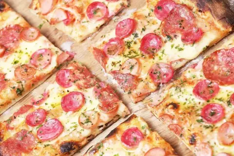 Kawałki pizzy z kiełbasą i serem, posypane ziołami. Idealne ciasto na pizzę dla każdego smakosza.