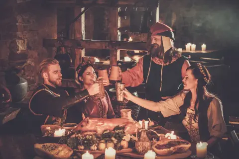 Ludzie w strojach z epoki wznoszą toasty przy suto zastawionym stole. To scena z historii piwa, gdzie napój ten towarzyszył ucztom od wieków.