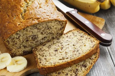Pyszny chlebek bananowy, pokrojony na kromki, z bananami i nożem na desce.