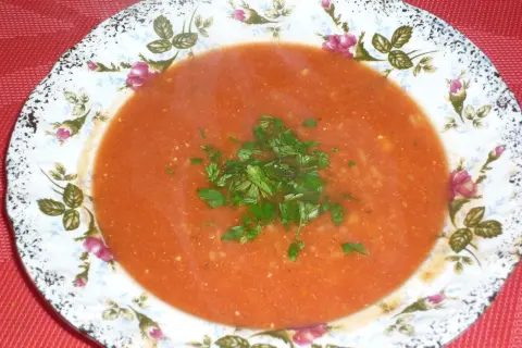 Aromatyczna zupa pomidorowa na bulionie warzywnym, udekorowana świeżą natką pietruszki, podana w ozdobnej porcelanowej misce.