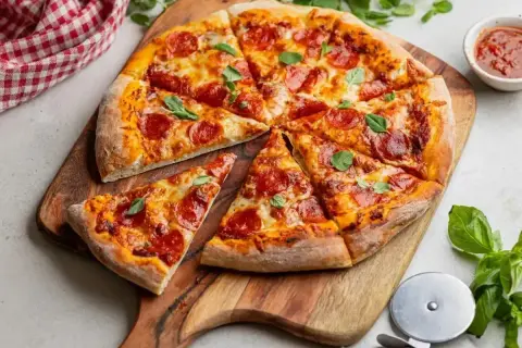 Pyszna pizza pepperoni, idealna na ostro, z ciągnącym się serem i świeżą bazylią, podana na drewnianej desce.