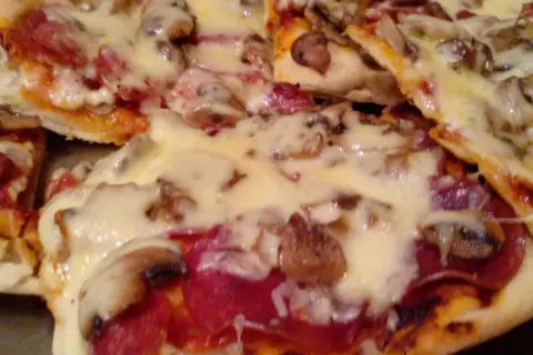 Pyszna domowa pizza z pieczarkami i salami, obficie posypana ciągnącym się serem. Idealna na wieczór z bliskimi.