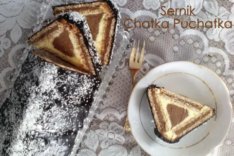 Sernik Chatka Puchatka, udekorowany czekoladą i wiórkami kokosowymi, wygląda pysznie. Kawałek na talerzyku zachęca do spróbowania.