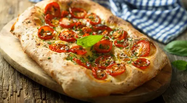 Pyszna focaccia z pomidorkami koktajlowymi i bazylią. Idealna jako przekąska, dodatek do sałatek lub jako samodzielne danie. Z czym jeść focaccię? Z tym, co lubisz!