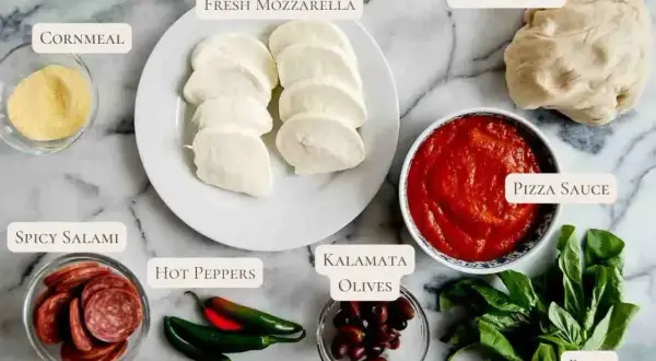 Składniki na pizzę z salami: ciasto, sos, mozzarella, oliwki, papryczki, bazylia i mąka kukurydziana.