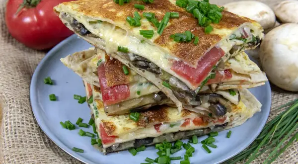 Pyszna tortilla na śniadanie z serem, pomidorami i grzybami, posypana szczypiorkiem.