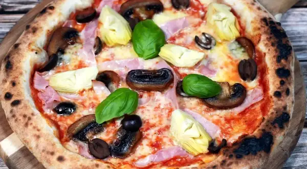 Pizza Capriciosa z klasycznymi składnikami: szynką, pieczarkami, karczochami i oliwkami.