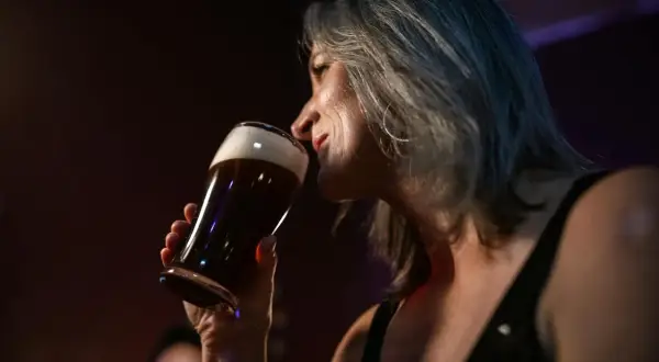 Kobieta z siwymi włosami wącha piwo. Czy piwo rozrzedza krew? Zastanawia się nad tym, delektując się napojem.
