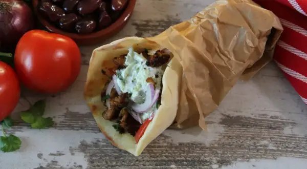 Pyszny pita gyros z soczystym mięsem, warzywami i kremowym sosem, obok pomidory, oliwki i cebula.