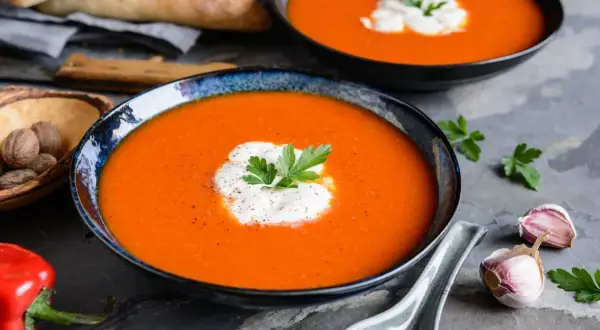 Aksamitny zupa krem z papryki, udekorowana śmietaną i natką pietruszki, podana z pieczywem i czosnkiem.