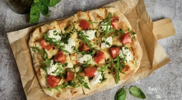 Pyszna pizza wege z pomidorami, mozzarellą i rukolą, polana zielonym pesto. Idealna na lekki posiłek.