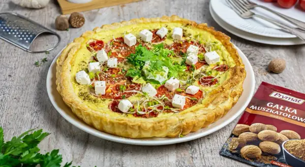 Tarta z pomidorami i kostkami sera mozzarella starta, ozdobiona kiełkami i ziołami.