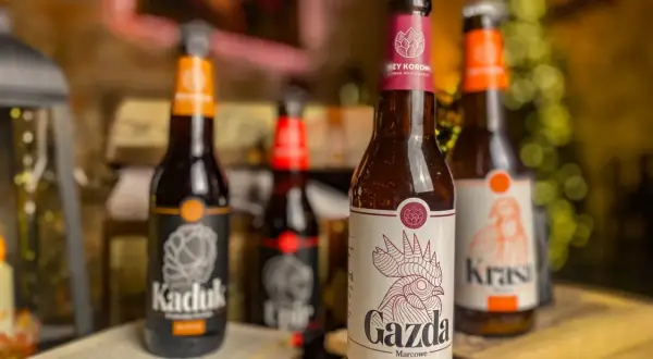 Piwo z Pomorza: butelki "Kaduk", "Gazda" i "Krasa" stoją na stole obok otwartej książki i szachownicy.