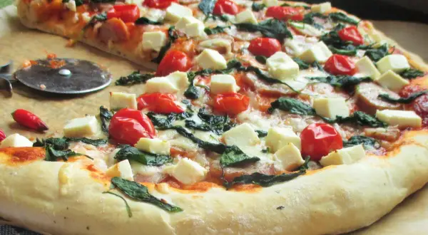 Pyszna pizza z fetą, pomidorkami koktajlowymi i szpinakiem, gotowa do pokrojenia.