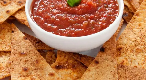 Chrupiące nachos otaczają miseczkę z aromatyczną, domową **salsą pomidorową**, ozdobioną listkiem pietruszki. Idealna przekąska!