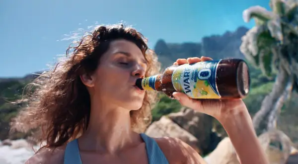 Kobieta pije piwo Zlatý Bažant 0,0% na plaży.