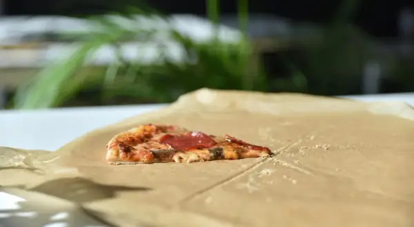 Kawałek pizzy z salami na śniadanie, leżący na papierze do pieczenia.