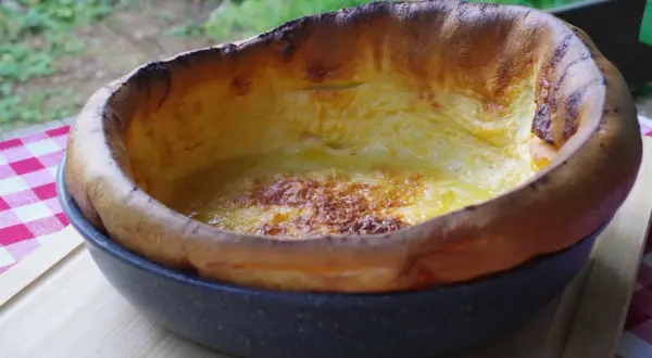Puszysty, złocisty dutch baby, lekko przypieczony na brzegach, w okrągłej formie.