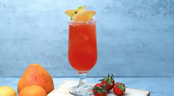 Orzeźwiający drink z pomarańczy i ananasa, z solą na brzegu kieliszka. Obok leżą truskawki, cytryna i pomarańcza. Idealny na lato, jak piwo cytrynowe.