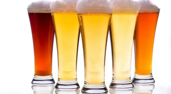 Pięć kielichów z piwem, w tym ciemny bursztynowy i jasny pilsner, z obfitą pianką.