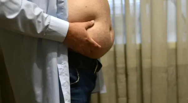Mężczyzna z dużym brzuchem od piwa, trzymający się za brzuch.