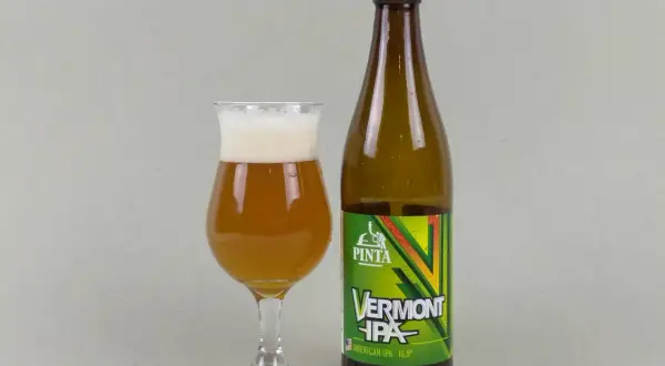Szklanka z bursztynowym piwem Vermont IPA i butelka tego piwa. Idealne neipa piwo na wieczór.