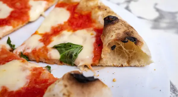 Kawałki pysznej pizzy neapolitańskiej z ciągnącym się serem i świeżą bazylią.