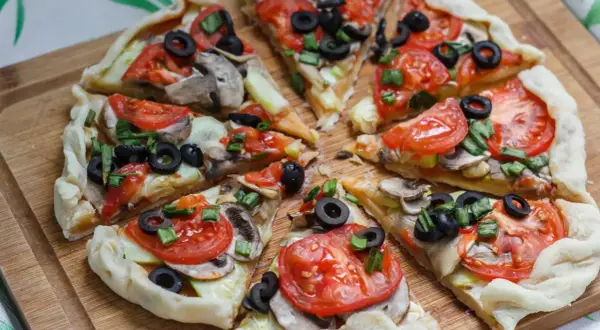 Kawałki pysznej, **zdrowej pizzy** z pomidorami, oliwkami i pieczarkami na drewnianej desce.