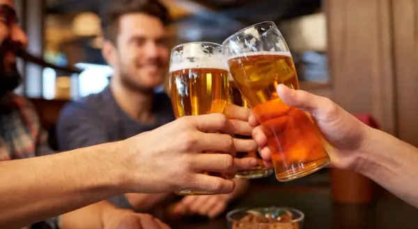 Trzech przyjaciół wznosi toasty. W rękach trzymają szklanki z bursztynowym piwem, a na stole stoi miseczka z orzeszkami. Idealny wieczór z piwem małym mocnym.