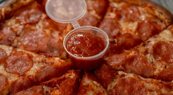 Pizza pepperoni z małym kubeczkiem sosu. Czy wolisz keczup czy ketchup?