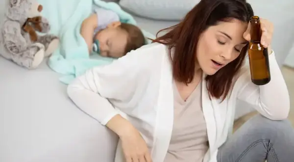 Zmęczona matka z butelką piwa obok śpiącego dziecka. Czy piwo karmi szkodzi?