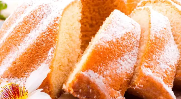Puszysta babka wielkanocna, oprószona cukrem pudrem, z kawałkami ciasta i kwiatową dekoracją.
