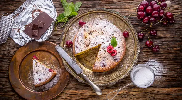 Pyszny kawałek ciasta drożdżowego z wiśniami, posypany cukrem pudrem. Idealny deser, choć warto pamiętać o jego kcal.