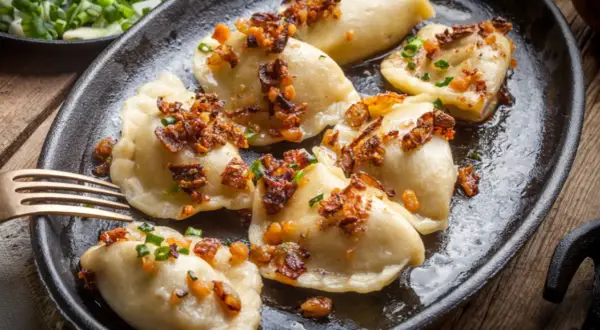 Pyszne pierogi z mięsem mielonym, okraszone skwarkami i szczypiorkiem, podane na żeliwnej patelni.
