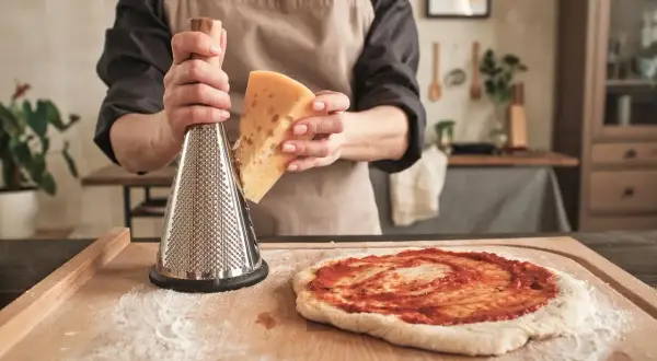 Osoba trze ser na pizzę. Zastanawiasz się, czy ciasto na pizzę może się zepsuć? Nie martw się, świeży ser to klucz do sukcesu!