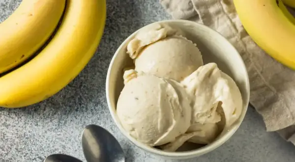 Pyszne lody bananowe w miseczce, obok świeże banany i łyżeczki. Idealne na upalny dzień.