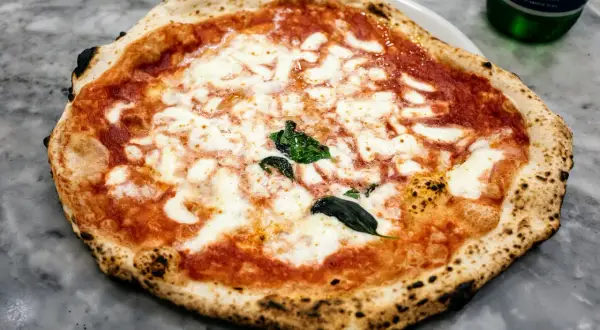 Nietypowa pizza margherita z lekko przypalonymi brzegami i świeżą bazylią, prezentująca się apetycznie na marmurowym blacie.