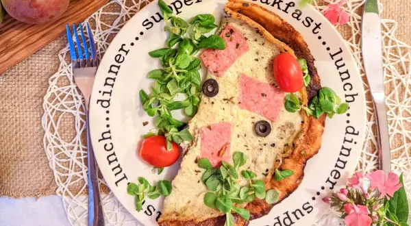 Pyszne, sycące śniadanie do pracy: omlet z szynką, pomidorkami i oliwkami, udekorowany świeżą sałatką.