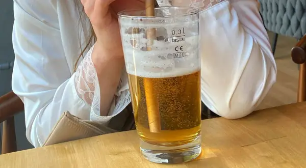 Szklanka złocistego piwa z pianką, idealna na trawienie. Ktoś w białej satynowej koszuli trzyma słomkę.